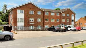 A multi-story brick building with a flat roof, several windows, and a parking area in front. - Lovely one bedroom flat (Wooburn Green, Bourne End)