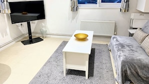 A modern living room with a flat-screen TV, a white coffee table with a bowl, a grey sofa, and a window with curtains. - Lovely one bedroom flat (Wooburn Green, Bourne End)