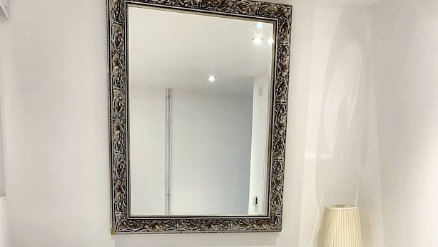 A bedroom with a large ornate mirror, a bed with white linens, and a bedside table with a lamp. - Lovely one bedroom flat (Wooburn Green, Bourne End)