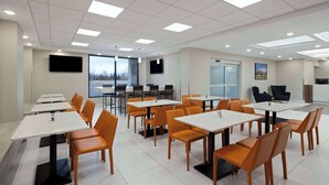 Un salón de conferencias con varias mesas y sillas, ventanas amplias y un televisor de pantalla plana montado en la pared.