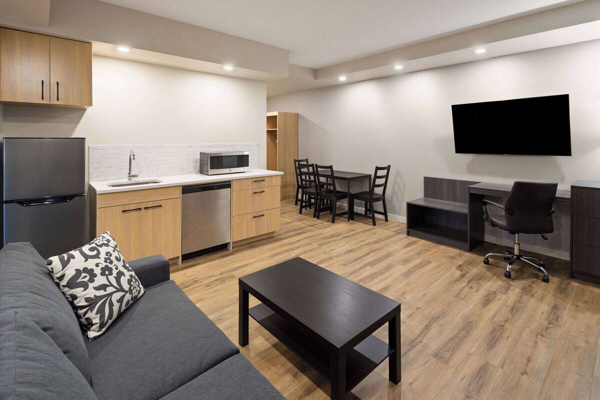 Een moderne woonkamer met een grijze bank, een houten eettafel en een flatscreen tv aan de muur.