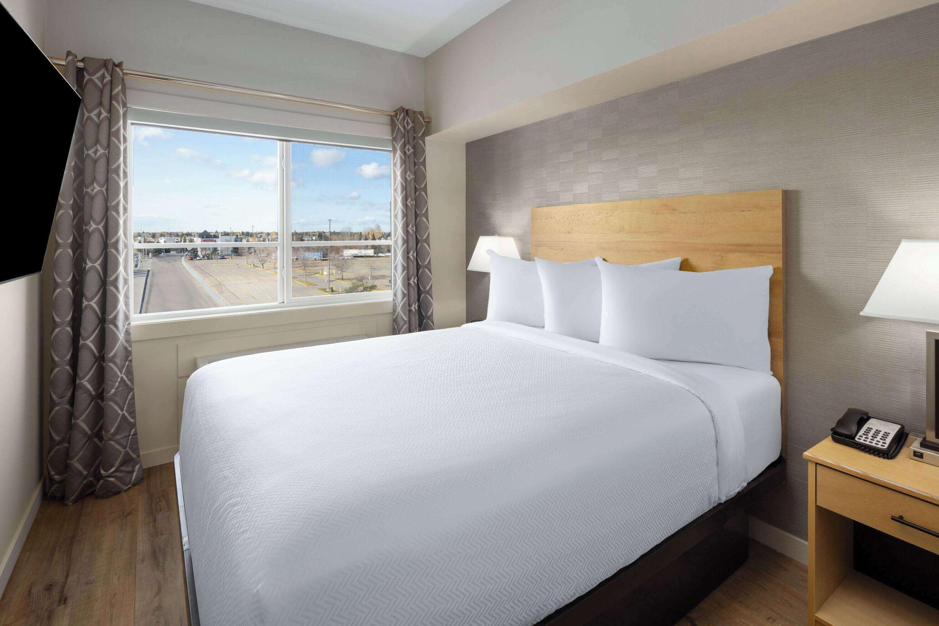 Habitación de hotel con una cama grande, una mesita de noche con lámpara, teléfono y ventana con cortinas.