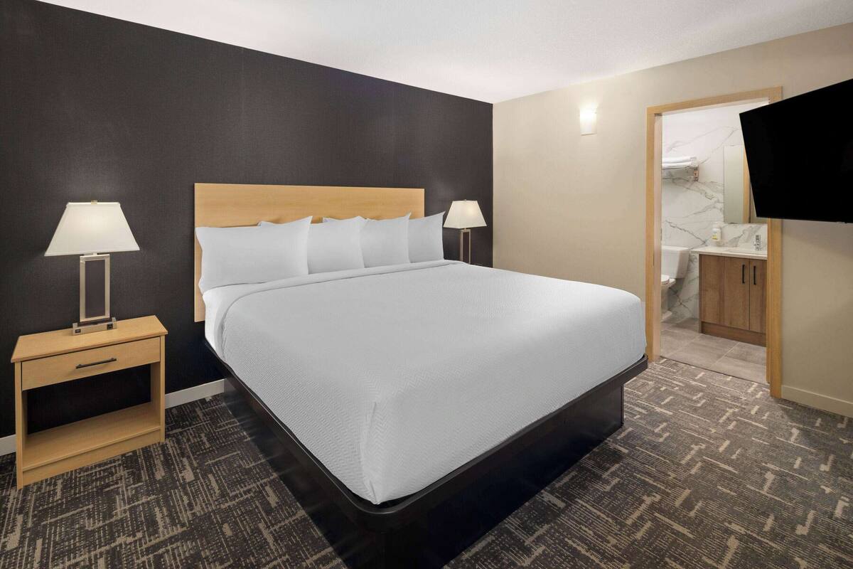 Een hotelkamer met een groot bed, twee nachtkastjes met lampen, een houten bijzettafeltje, een aan de muur bevestigde televisie en een badkamer zichtbaar door een geopende deur.
