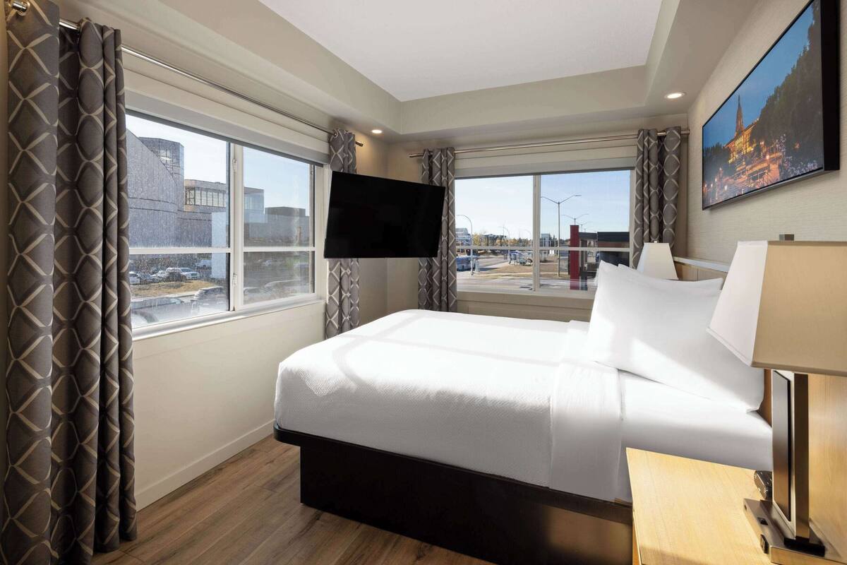 Hotelkamer met een groot bed, een aan de muur bevestigde televisie en een uitzicht op de stad door de ramen.