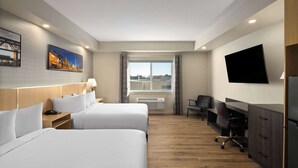 Habitación de hotel con dos camas, un escritorio, una silla, un televisor y una ventana con cortinas.