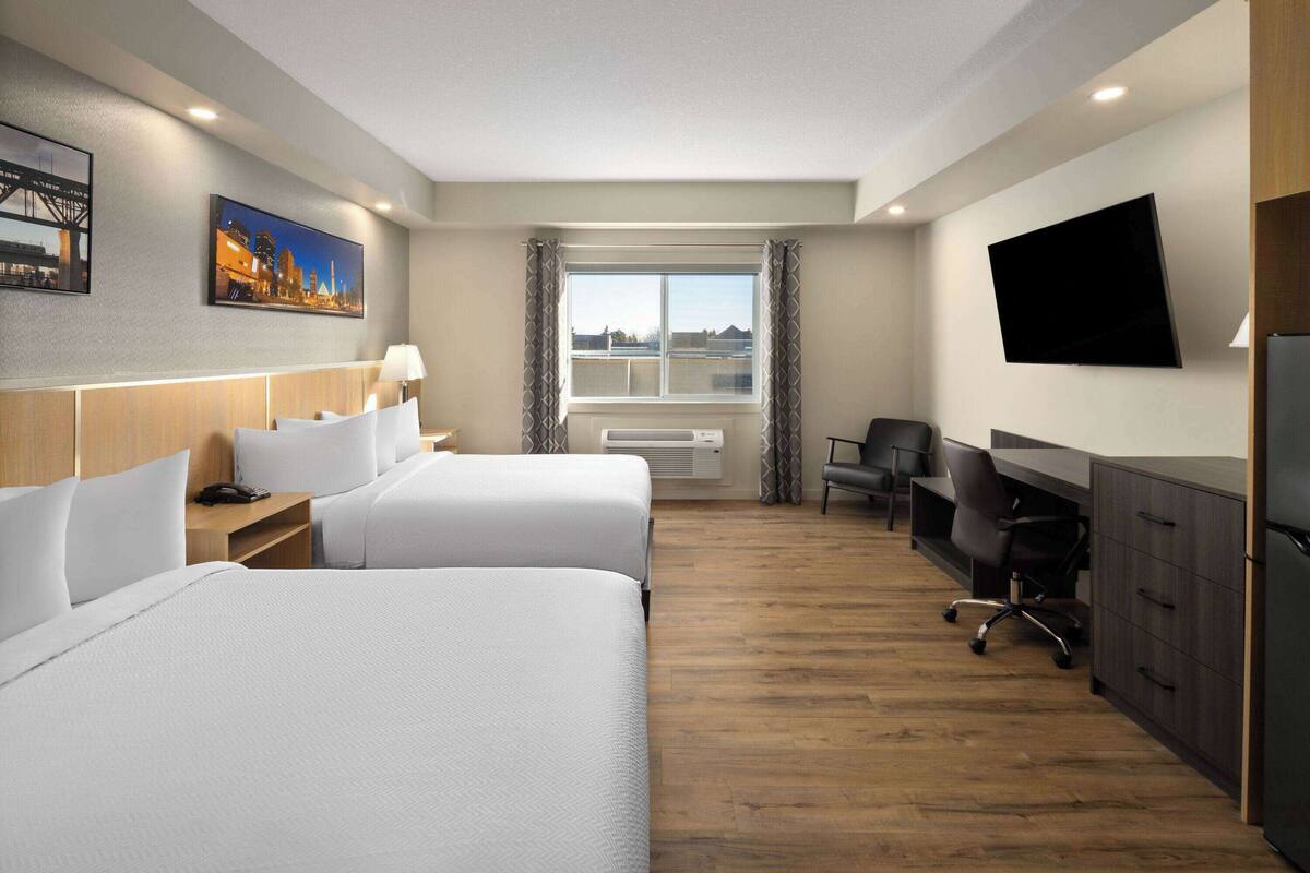 Een hotelkamer met twee bedden, een bureau, een stoel, een televisie en een raam met gordijnen.