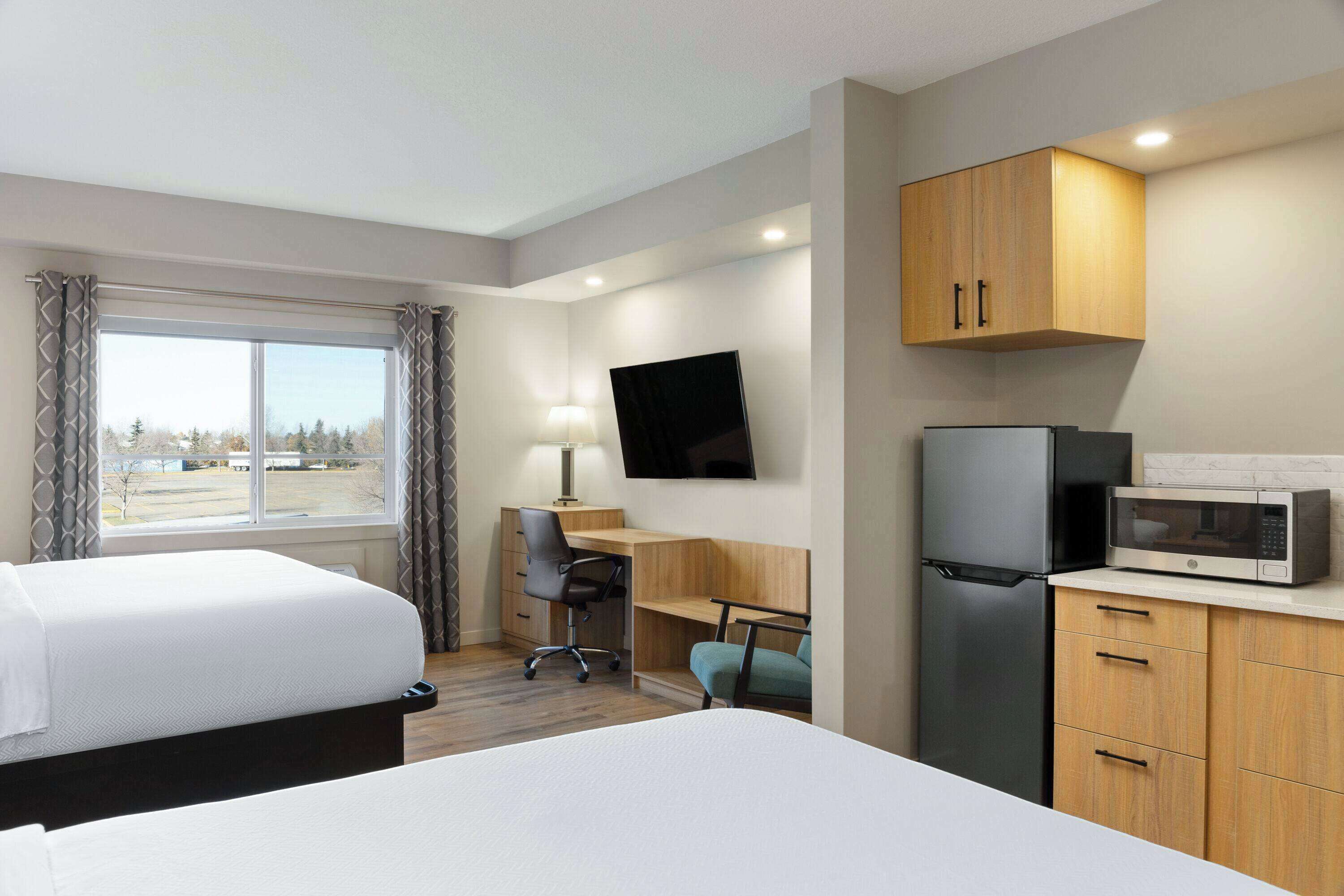 Une chambre d’hôtel équipée d’un lit, d’un bureau, d’une chaise, d’une télévision, d’un réfrigérateur, d’un four à micro-ondes et d’armoires en bois.