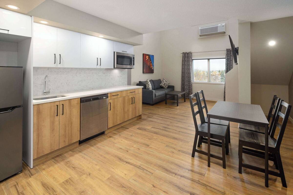 Een moderne keuken met houten kastjes, een ingebouwde magnetron en een vaatwasser. Er is een eethoek met een tafel en stoelen.