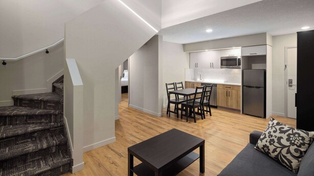 Un apartamento moderno con una escalera que conduce a un dormitorio tipo loft, un comedor con mesa y sillas, y una cocina equipada.