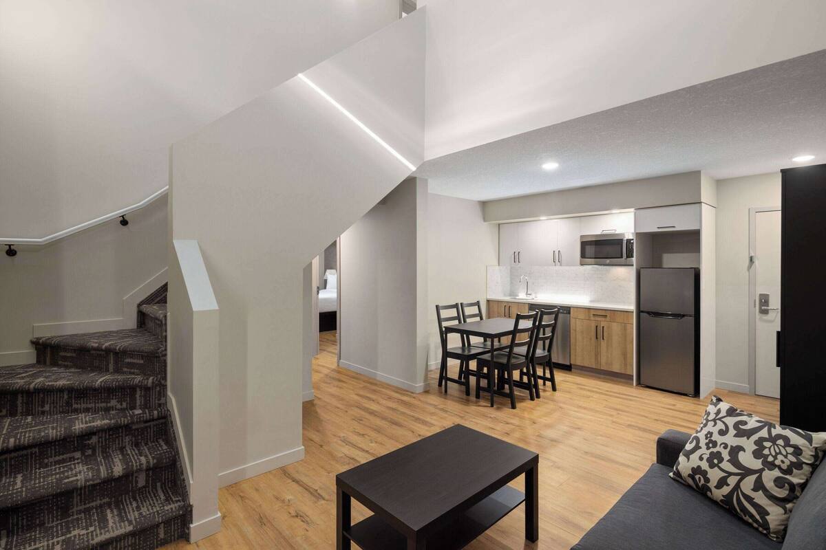 Een modern appartement met een trap naar een slaapkamer op een entresol, een eethoek met tafel en stoelen, en een keuken met apparatuur.