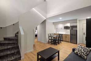 Un apartamento moderno con una escalera que conduce a un dormitorio tipo loft, un comedor con mesa y sillas, y una cocina equipada.