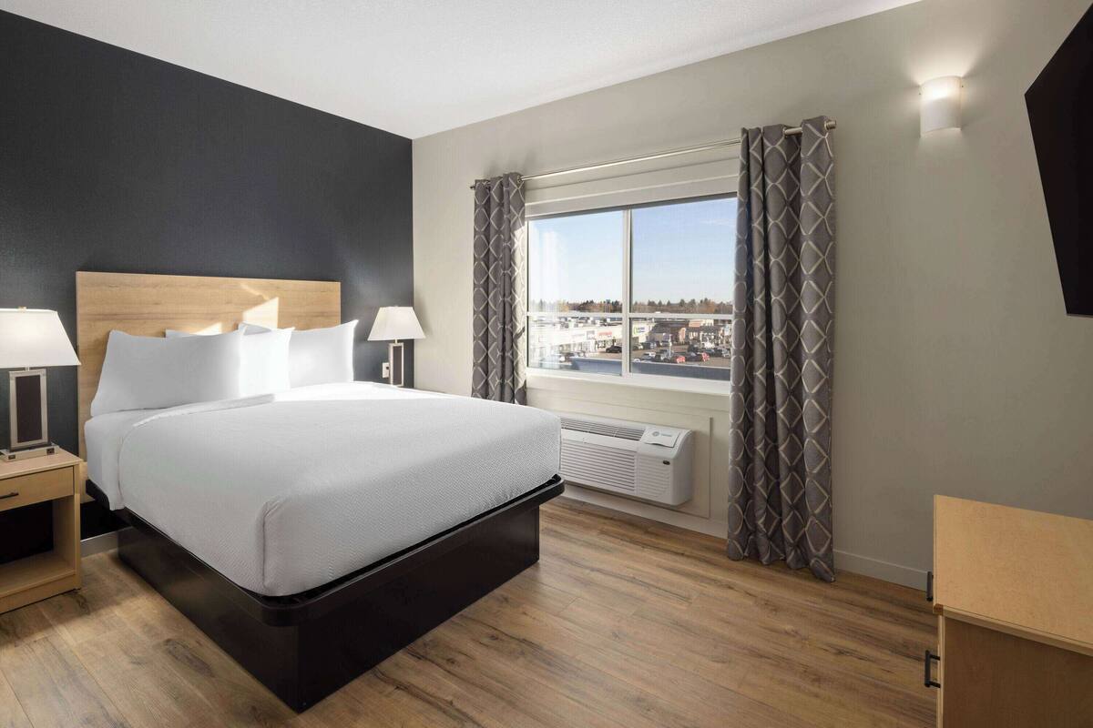 Een moderne hotelkamer met een groot bed, bedlampen, een raam met gordijnen en uitzicht op de stad.