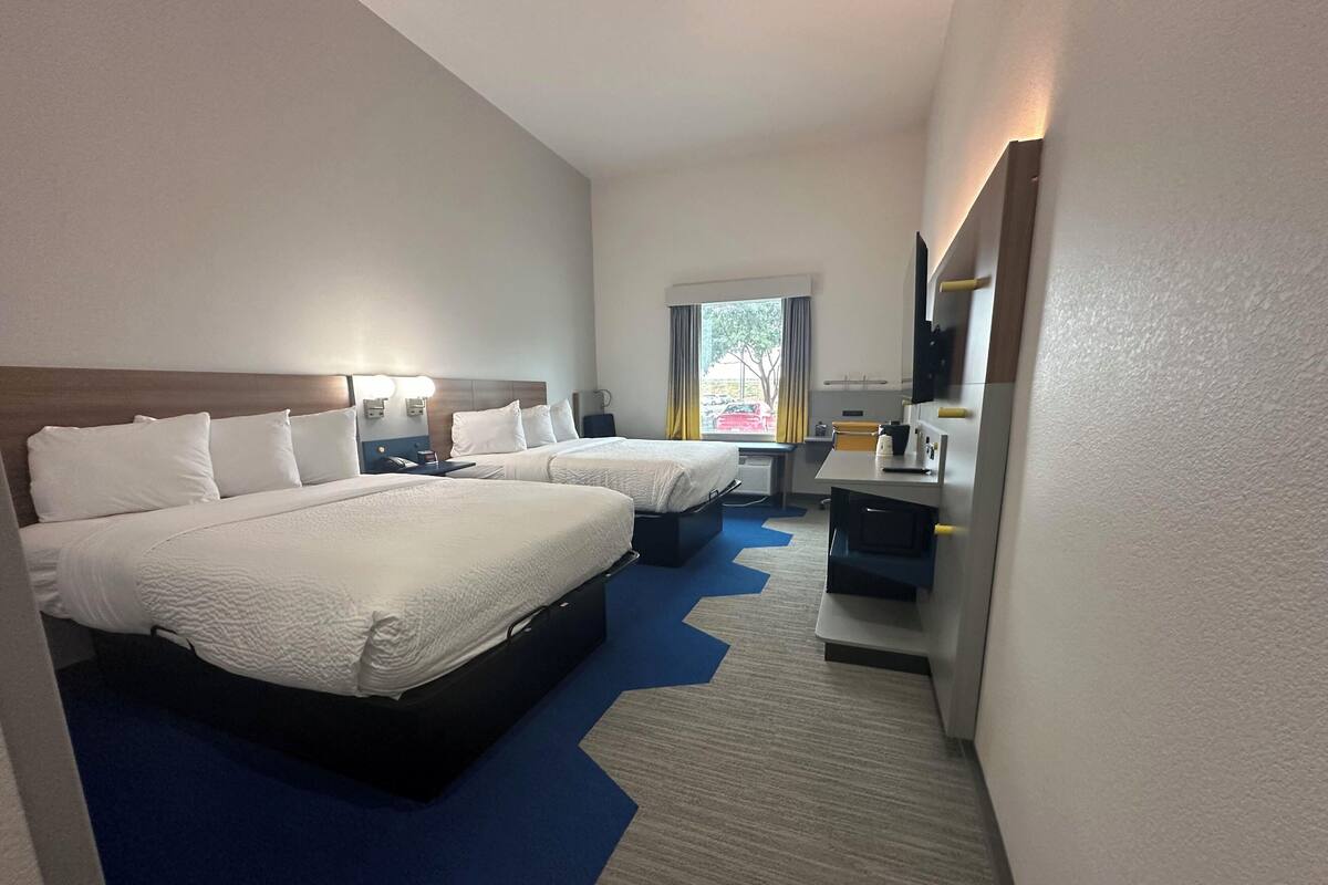 A hotel room with two beds, a desk, a chair, a mirror, and a window with curtains.