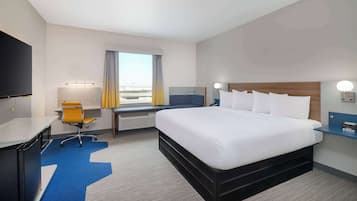 A hotel room with a large bed, a desk with a chair, a TV, a window with curtains, and a view of the city.