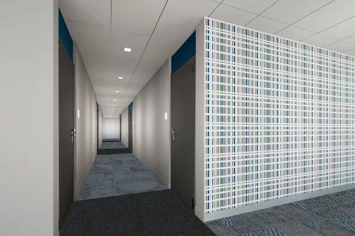 A corridor with a patterned carpet, white walls, and a white partition with a grid design.