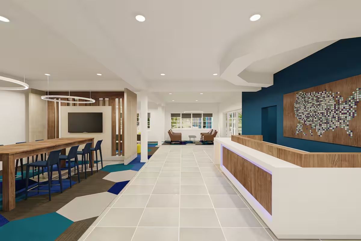 A modern hotel lobby with a reception desk, seating area, and a large wall art piece.