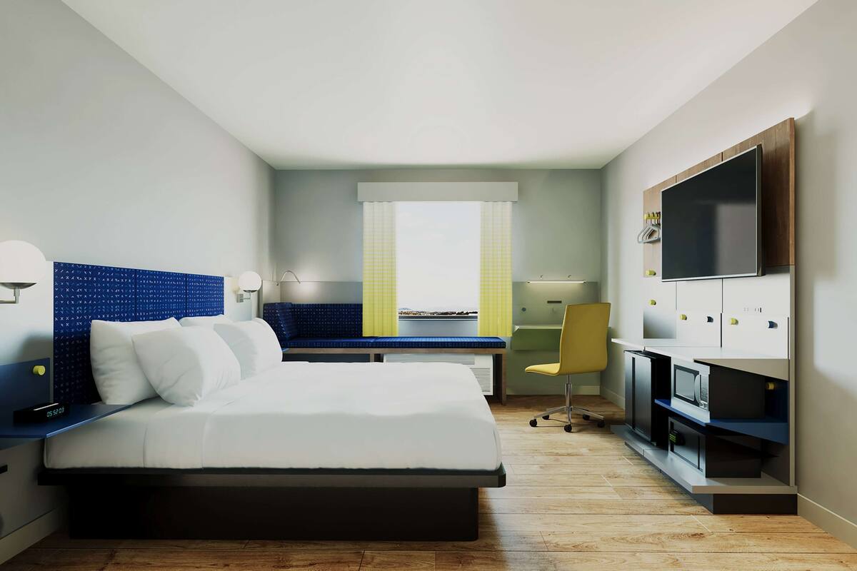 A modern hotel room with a bed, desk, chair, TV, and storage cabinets.