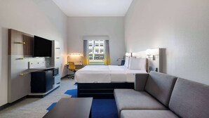 A hotel room with a bed, a sofa, a desk, a TV, and a window with curtains. - Microtel Inn & Suites By Wyndham Amarillo West (Amarillo)