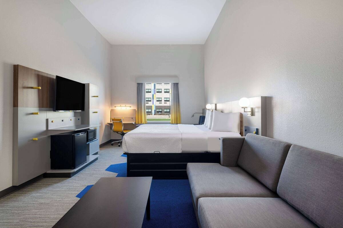 A hotel room with a bed, a sofa, a desk, a TV, and a window with curtains.