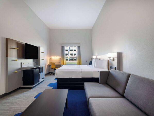 A hotel room with a bed, a sofa, a desk, a TV, and a window with curtains.