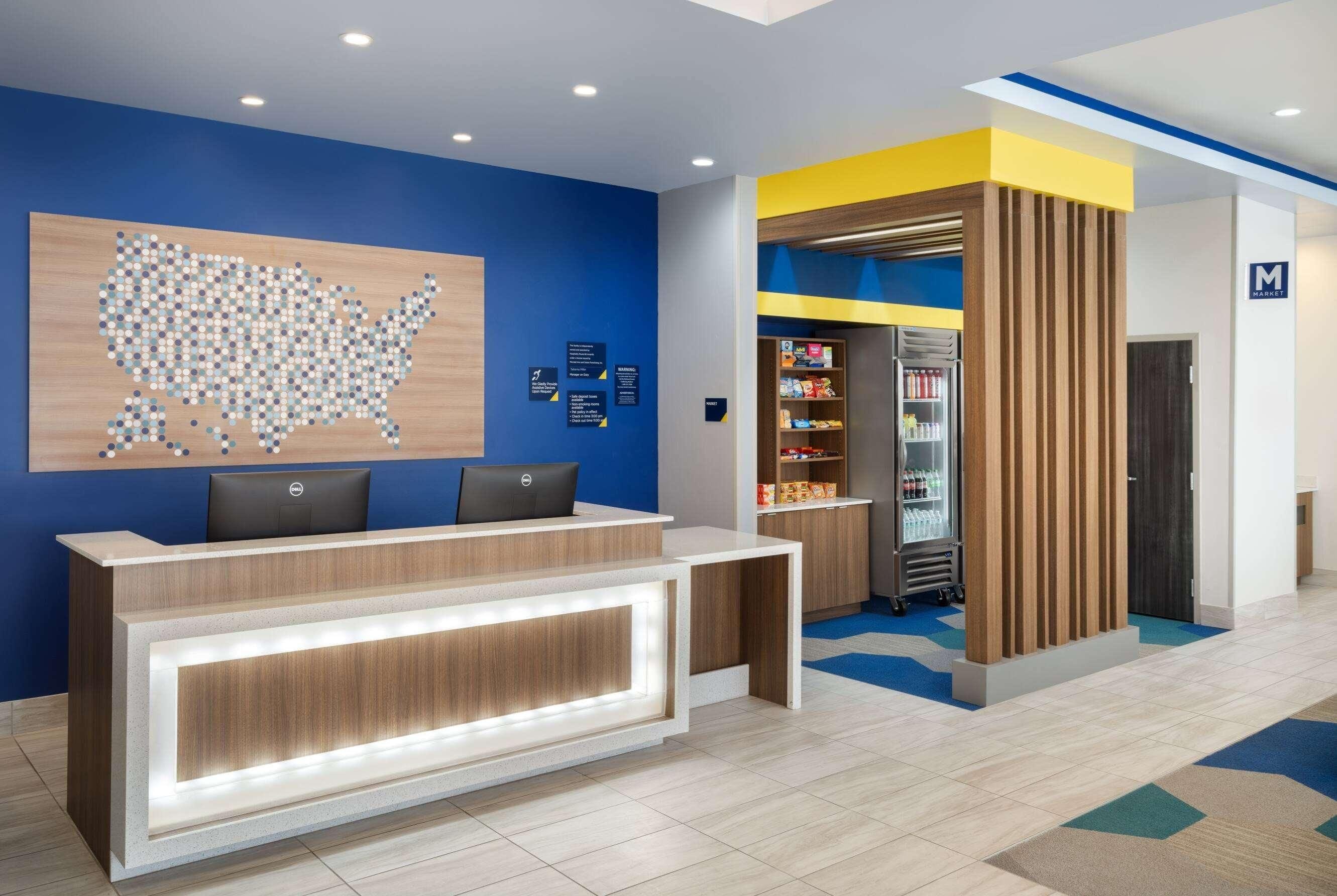 A hotel reception area with a desk, two chairs, a wall map, and a refrigerator stocked with beverages.