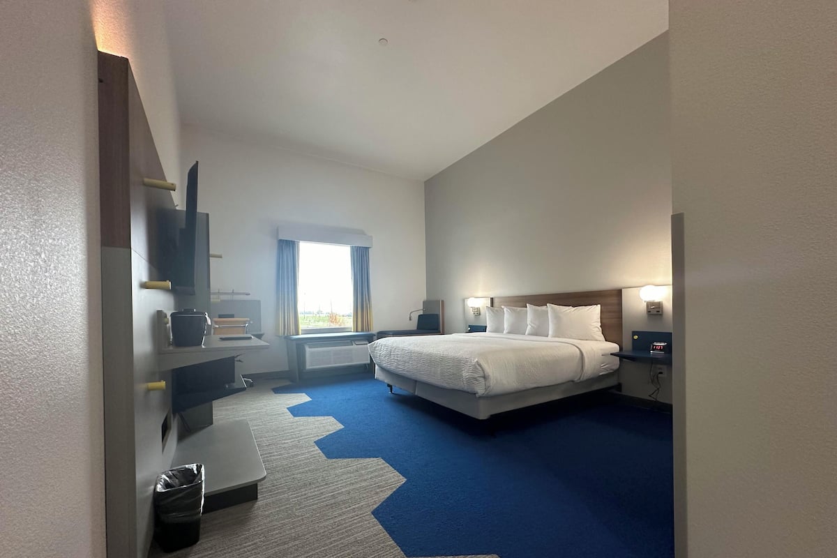 A hotel room with a large bed, a desk, a chair, a TV, and a window with curtains.