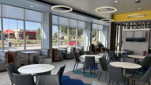 A modern indoor seating area with round tables and chairs, large windows offering a view of the outside, and a flat-screen TV mounted on the wall. - Microtel Inn & Suites By Wyndham Amarillo West (Amarillo)