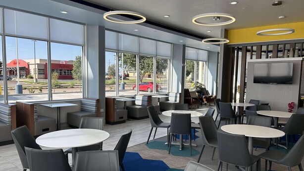 A modern indoor seating area with round tables and chairs, large windows offering a view of the outside, and a flat-screen TV mounted on the wall. - Microtel Inn & Suites By Wyndham Amarillo West (Amarillo)