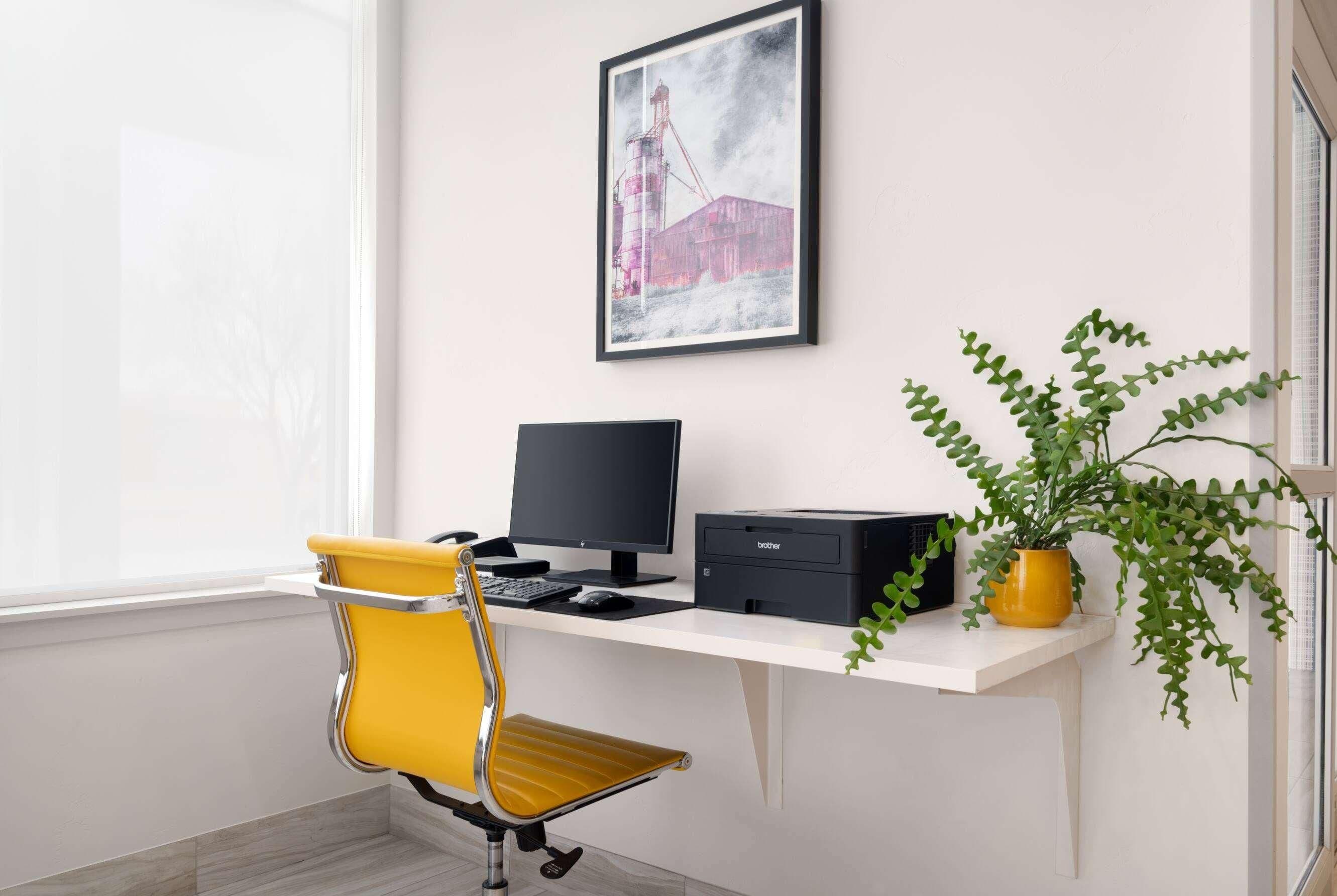 A workspace with a desk, a computer, a printer, a yellow chair, and a potted plant.