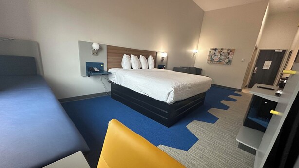 A hotel room with a bed, bedside table, lamp, and a desk with a chair. - Microtel Inn & Suites By Wyndham Amarillo West (Amarillo)