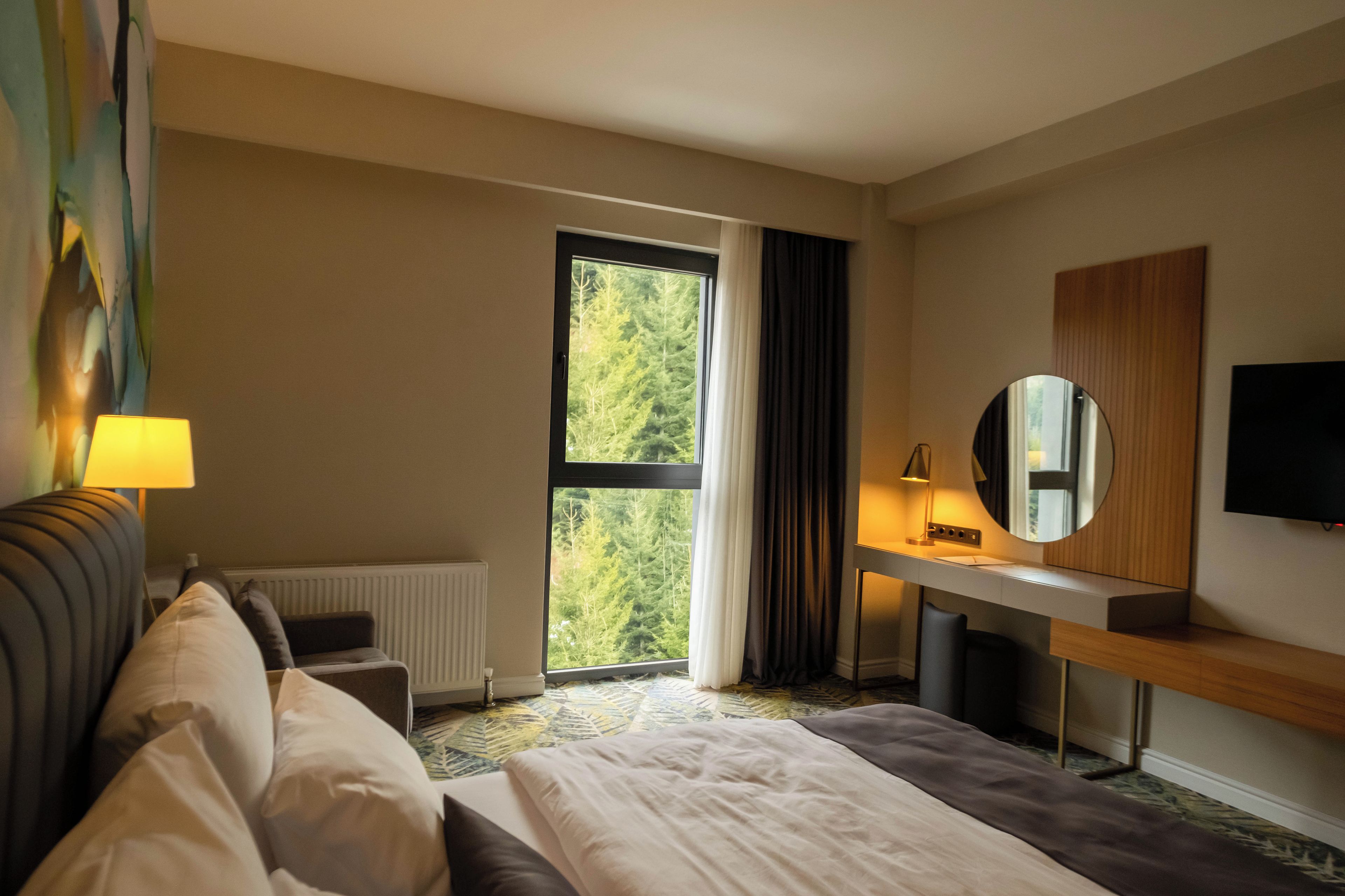 A hotel room with a bed, a desk, a chair, a TV, and a window with curtains.