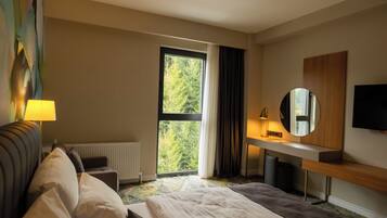 A hotel room with a bed, a desk, a chair, a TV, and a window with curtains.