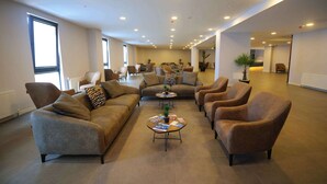 Amplia sala de estar con sofás y sillones dispuestas alrededor de una mesa central, un gran ventanal que aporta luz natural y una puerta que da a otra habitación.