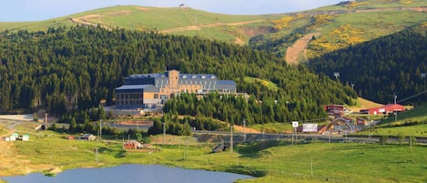 A large building with multiple floors, surrounded by a lake and forested hills.