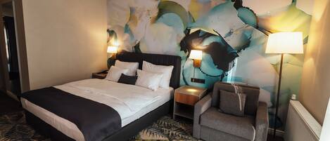A hotel room with a large bed, two bedside tables with lamps, a chair, and a colorful abstract wall mural.