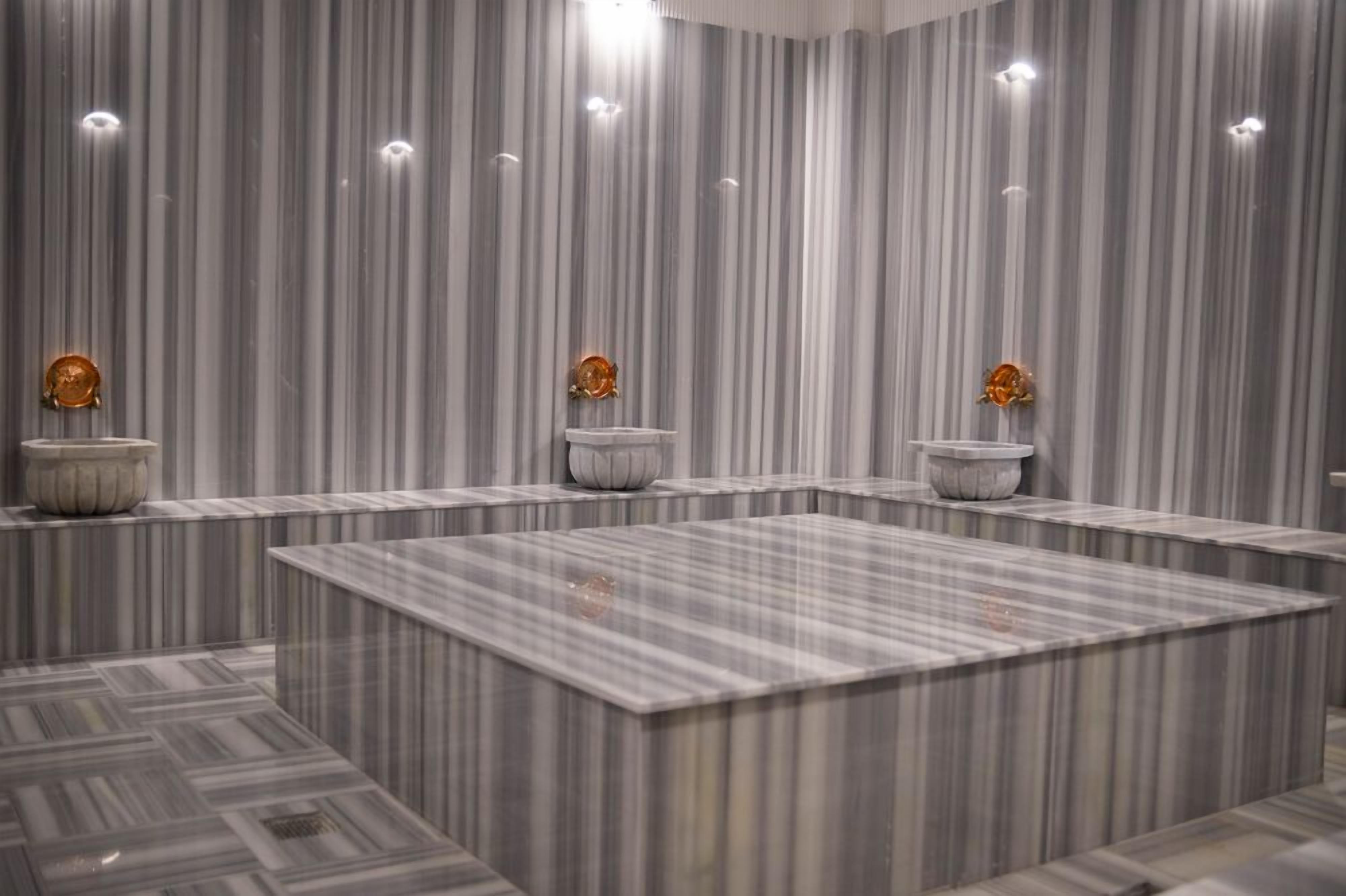 A modern bathroom with marble walls and floors, a central square sink, and decorative wall sconces.
