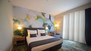 Habitación de hotel con una cama grande, dos lámparas de noche, una mesita de noche, una silla y un cuadro abstracto de gran tamaño en la pared.