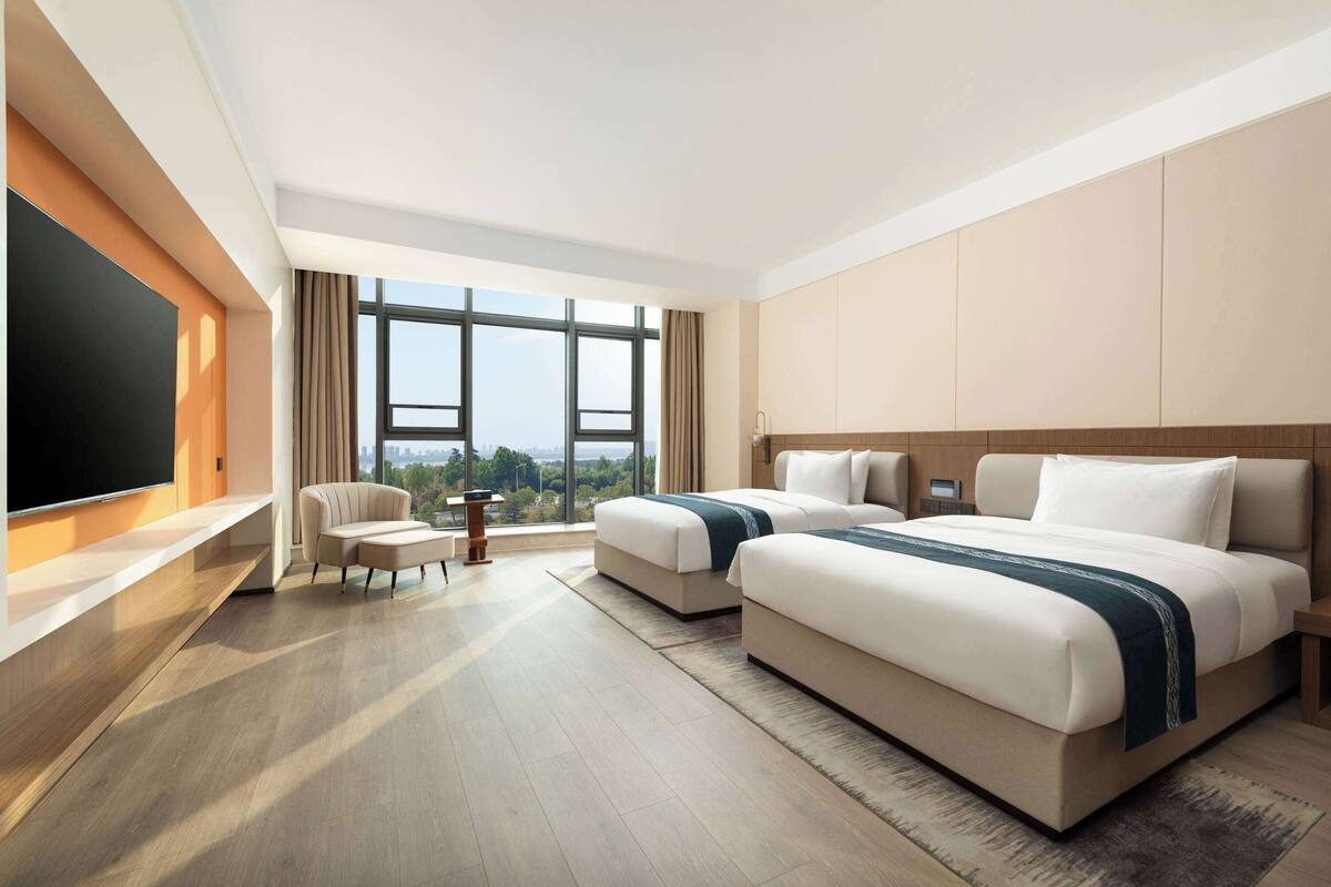Ein modernes Hotelzimmer mit einem großen Bett, einer Couch, einem Fernseher und Blick auf die Stadt.