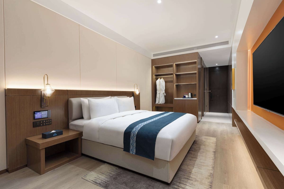 Ein modernes Hotelzimmer mit einem großen Bett, Nachttischen, einem Fernseher und einem Kleiderschrank.