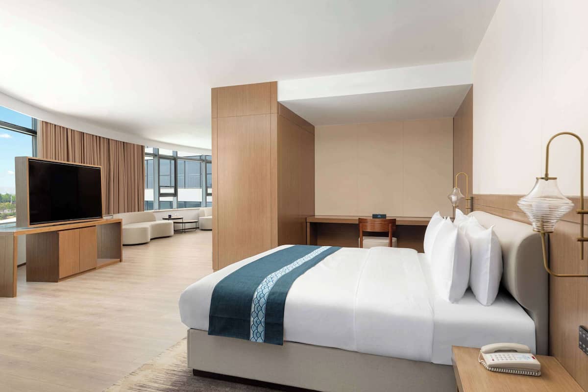 Ein modernes Hotelzimmer mit einem großen Bett, einem Flachbildfernseher, einem Schreibtisch und einer Sitzecke mit Sofa und Sesseln.