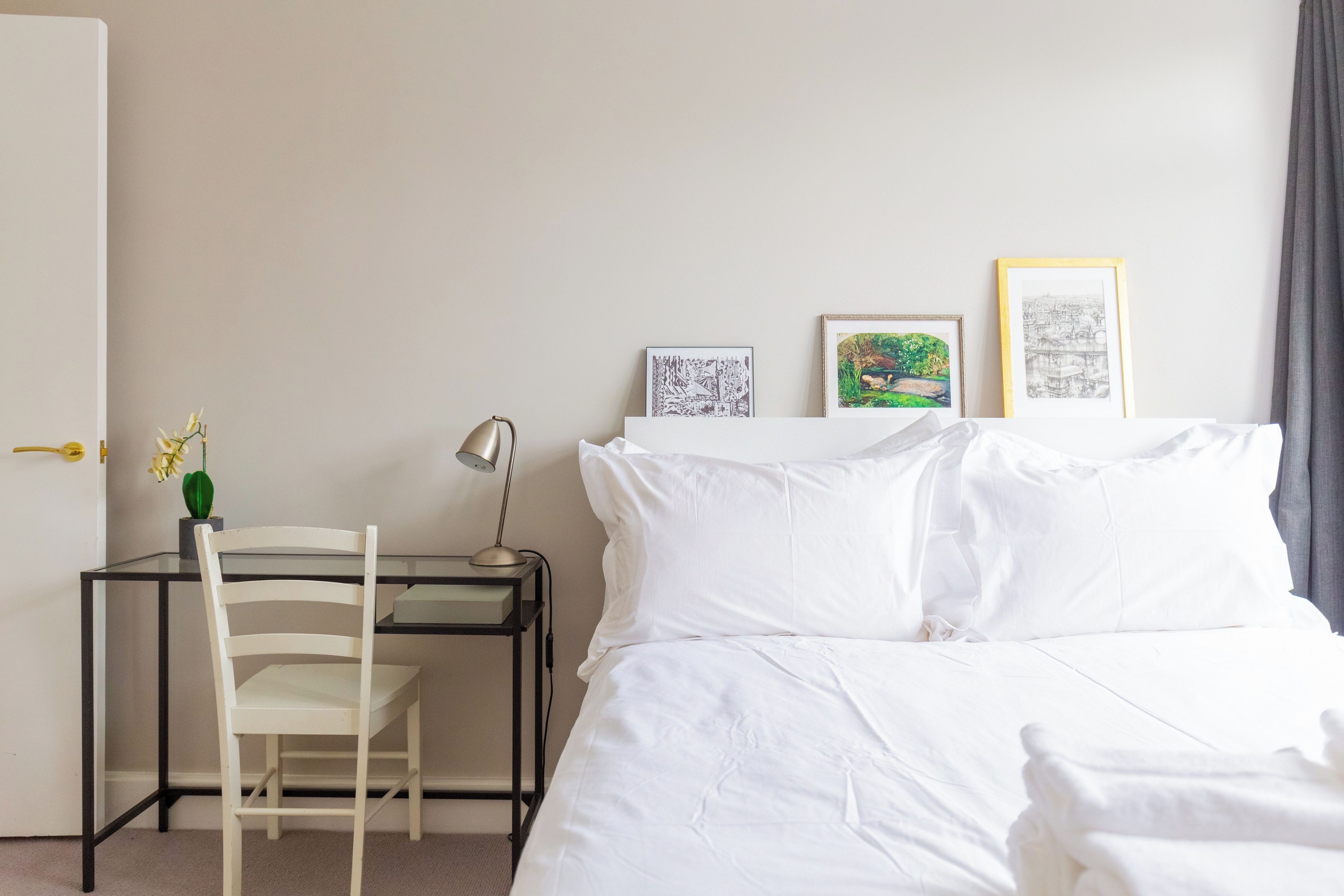 Habitación de hotel con cama, escritorio con silla, lámpara y tres cuadros en la pared.