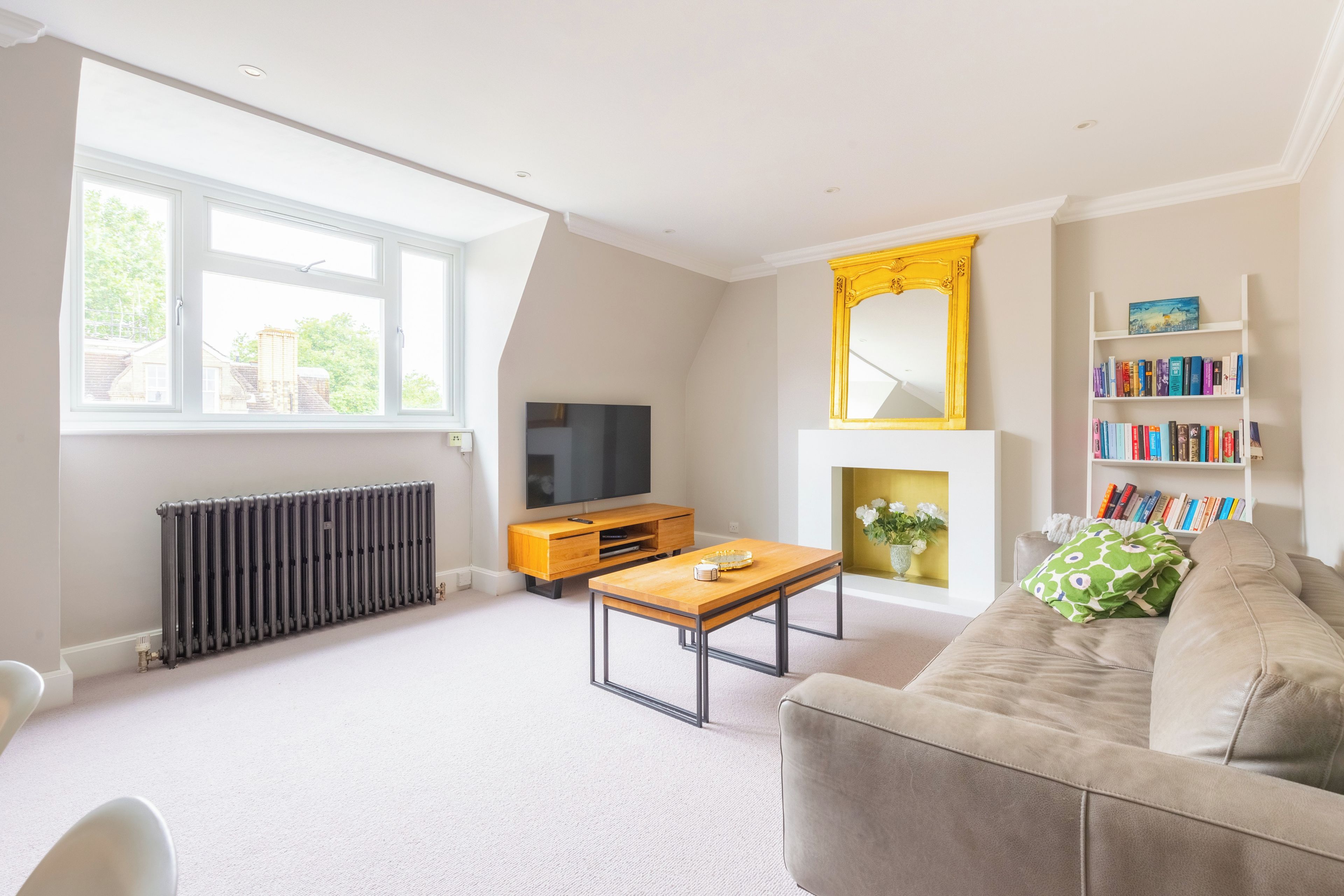 A modern living room with a sofa, coffee table, TV, fireplace, bookshelf, and a radiator.