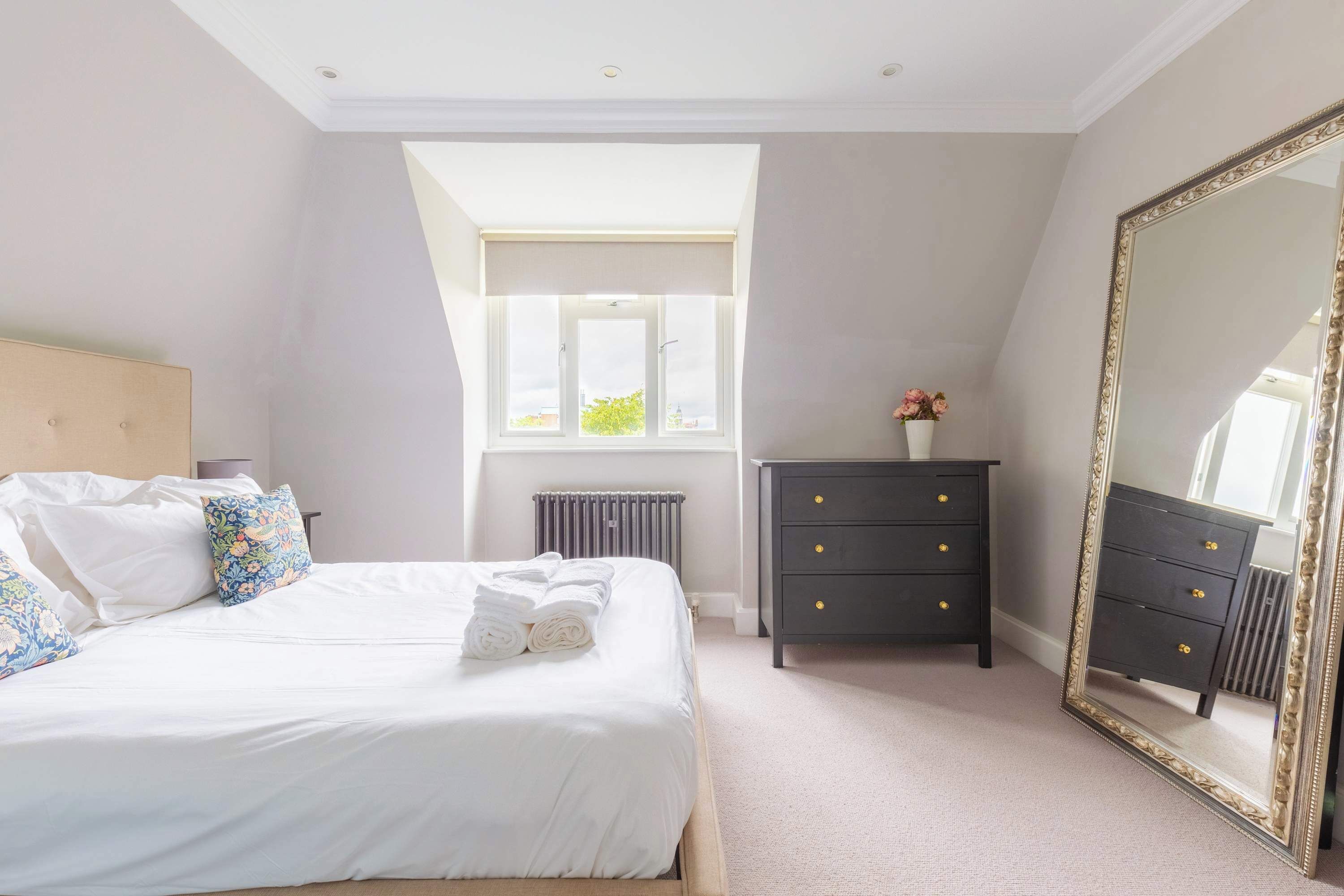 A bedroom with a bed, a dresser, a mirror, a radiator, and a window.