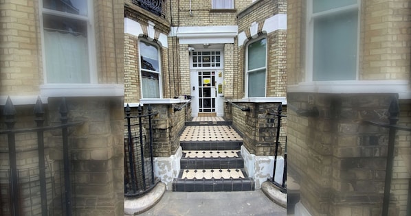 A narrow stairway leading to a door with a number plate, flanked by brick walls and metal railings.