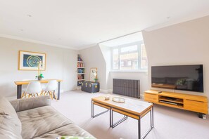 A living room with a sofa, a coffee table, a TV, a bookshelf, and a dining area with chairs and a table.
