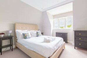 Une chambre à coucher comprenant un lit, des tables de chevet, une commode, un radiateur et une fenêtre donnant sur un paysage agréable.