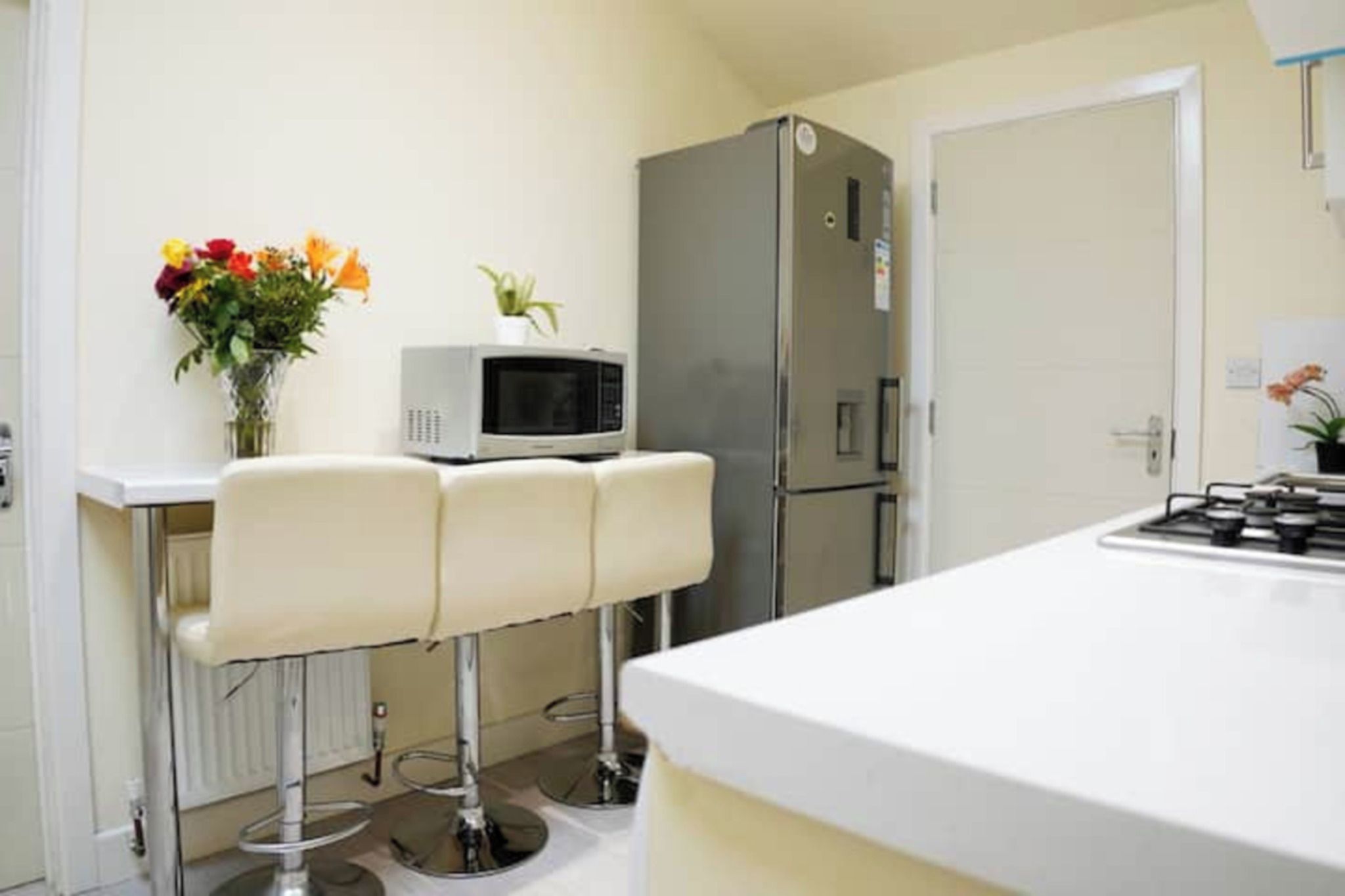 Una cocina con encimera blanca, microondas, refrigerador y un taburete de bar.