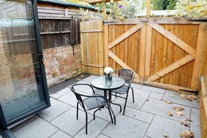 Eine Terrasse mit Glastür, einem runden Tisch und zwei Stühlen.