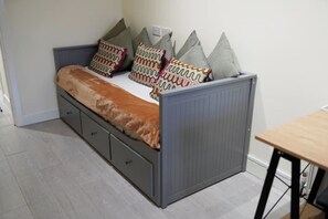 Ein kleines Bett mit Stauraum Schublade darunter, graue Kopfteil und gemusterte Kissen.