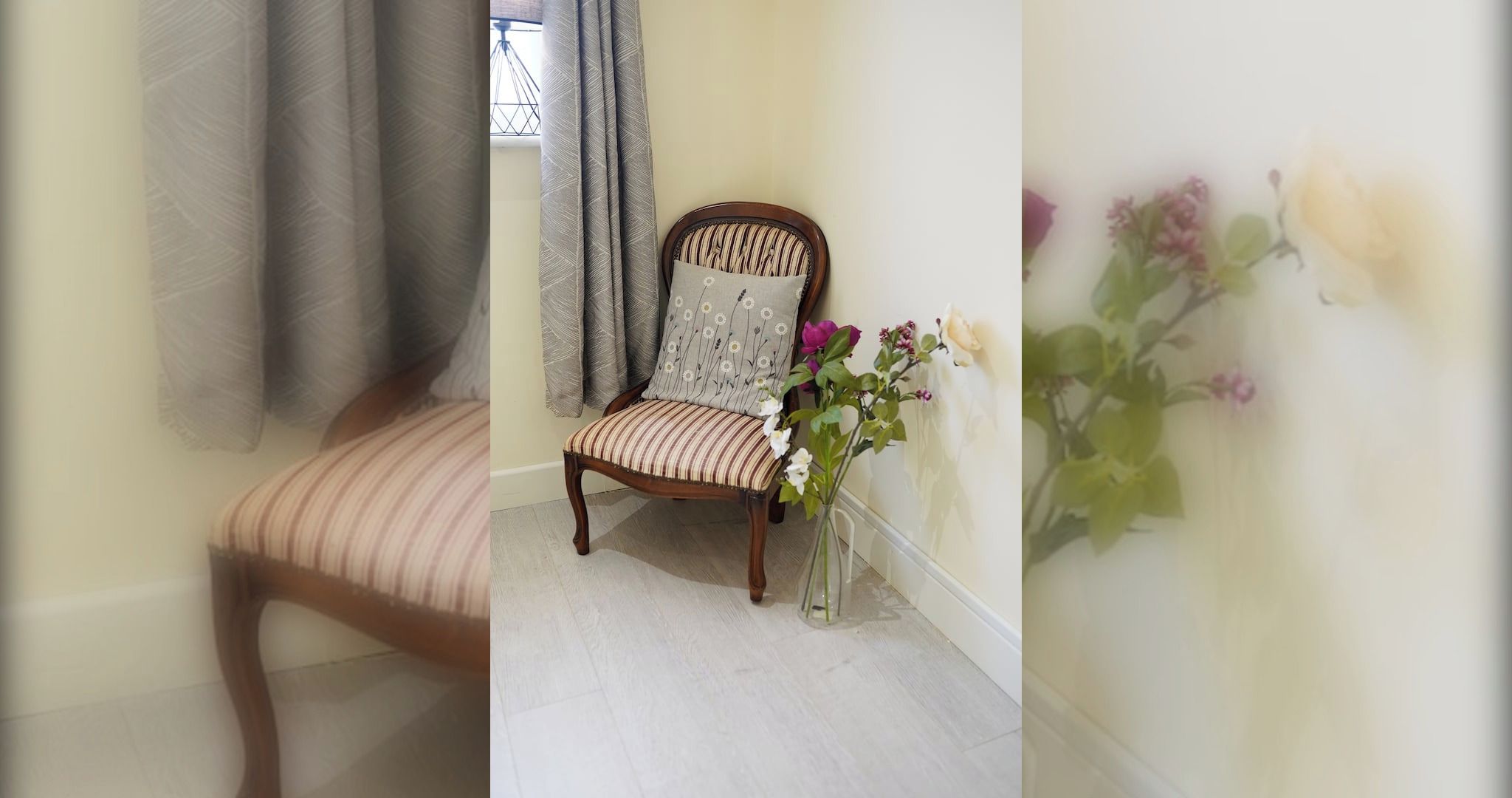 Een kamer met een houten stoel, een klein tafeltje en een vaas met bloemen.